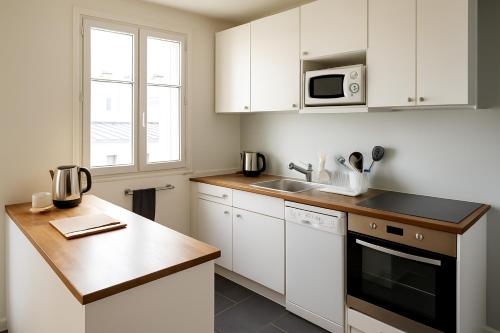 une cuisine avec des armoires blanches, un évier et un micro-ondes dans l'établissement Sunny Serenity: 2-room Charm in Boulogne, à Boulogne-Billancourt