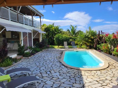 a swimming pool in a yard with chairs and a house at Fleur de canne in Sainte-Rose