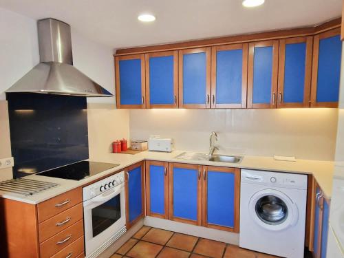 a kitchen with blue cabinets and a washing machine at Apartamentos Turisticos CAN CUNILL in Es Pujols