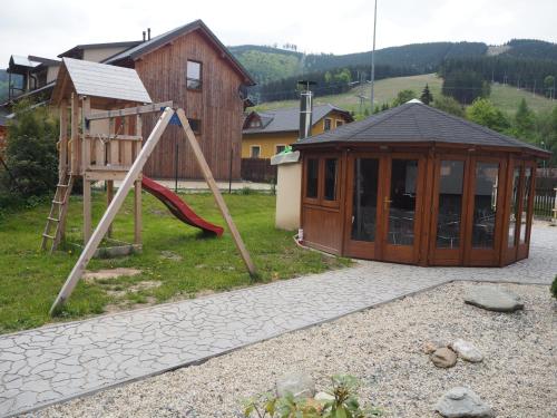 a playground with a wooden house and a slide at S4 Resort Kouty in Loučná nad Desnou