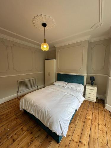 a bedroom with a large white bed and wooden floors at Stylish Four-Bed Haven Near Greenwich in Plumstead