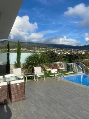 a patio with white chairs and a swimming pool at Vila Da Luz Calheta in Estreito da Calheta