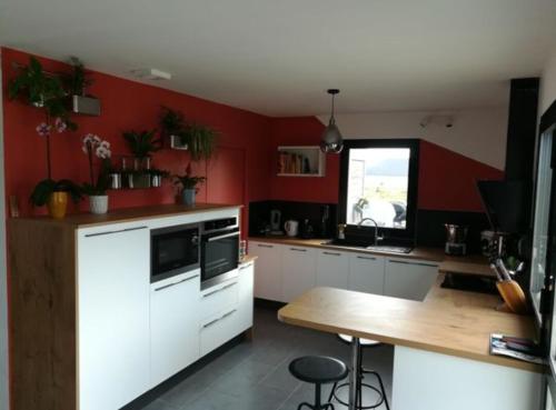 une cuisine avec des murs rouges et des armoires blanches et une table en bois dans l'établissement Maison de famille, 5min des plages, à Saint-Alban