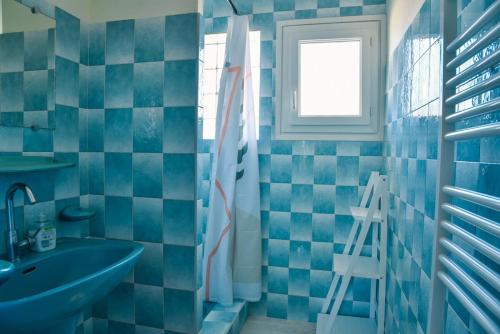 La salle de bains est pourvue de carrelage bleu, d'un lavabo et d'une fenêtre. dans l'établissement Les Tourterelles, à Seignosse