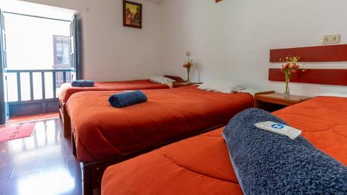 a room with three beds with orange sheets at La Estación San Pedro in Cusco