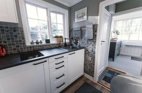 a kitchen with white cabinets and a sink and windows at Serene lakeside cabin next to the sea just 10 minutes from Stockholm city in Solna