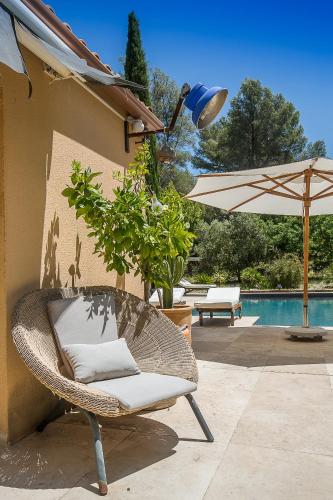 une chaise en osier et un parasol à côté d'une piscine dans l'établissement Villa Des oliviers, au Beausset
