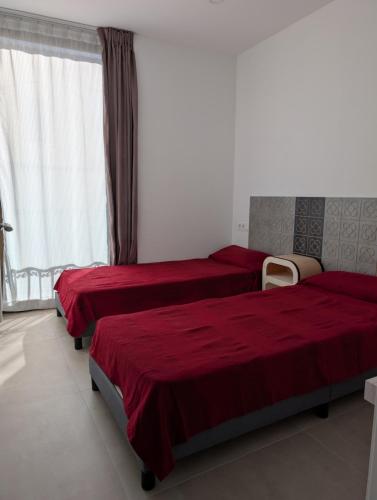 two beds in a bedroom with red sheets and a window at Ca l'Emília, hasta 6 pers, Monistrol de Montserrat in Monistrol