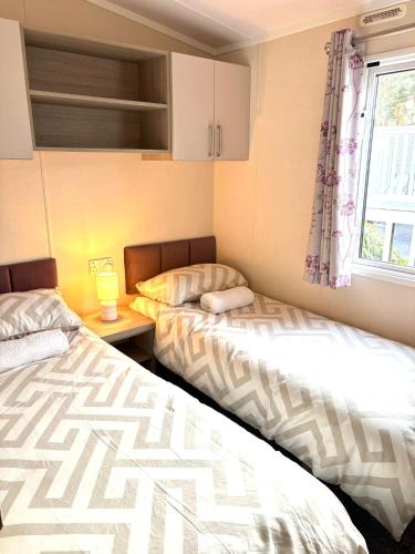 two beds in a small room with a window at 2 Bed, 2 Bathroom, modern Caravan with Sea views! in Lytchett Minster