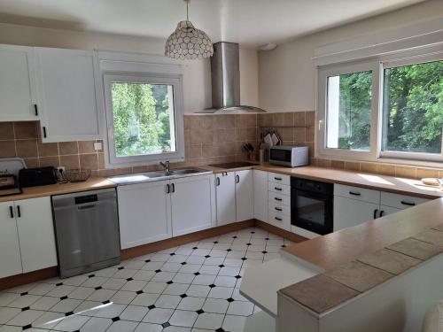 La cuisine est équipée de placards blancs, d'un évier et de fenêtres. dans l'établissement Maison à 5 minutes de la plage à pied, à Binic