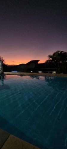 a large swimming pool with a sunset in the background at Rancho do Veio - Jarinu in Jarinu