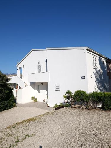 a white building with a gravel driveway at Apartments Višnja in Pag