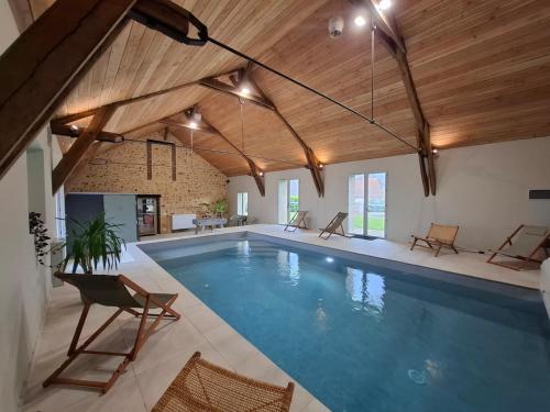 une grande piscine avec un plafond en bois dans l'établissement La Grange Flor'Alie gîte et piscine intérieure, à Meslay-le-Grenet