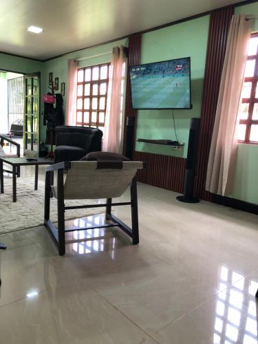 a living room with a flat screen tv and a chair at Casita Canto del Bosque Monteverde in Tilarán