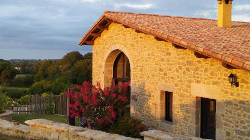un bâtiment en pierre avec un buisson à fleurs rouges à côté dans l'établissement Gîte Le Bouton d'Or 3 étoiles 8 kms PuyDuFou, à Chambretaud