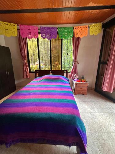 a bedroom with a bed with a colorful blanket on it at La Casa De Los Sueños Colombia Hostel Campestre Temático Ancestral in Ibagué