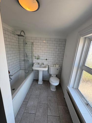 a bathroom with a toilet and a tub and a sink at Spacious 4-Bed Home R&B STAYS Welcomes You in Eastbourne