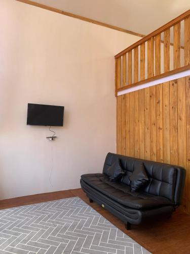 a black leather couch in a room with a television at Cabin wahyu abadi near prau Mountain type mezzanine in Dieng
