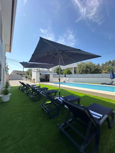 a row of lounge chairs with an umbrella next to a pool at Alojamento Rio Neiva in Boticas