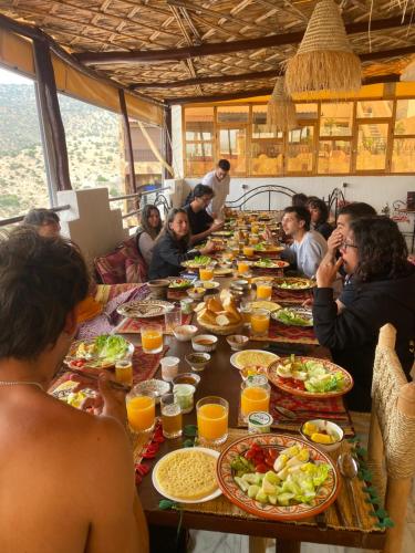 a group of people sitting around a long table with food at RED CARPET SURF CAMP - Traditional Moroccan GuestHouse With Stunning Views in Tamraght Ouzdar