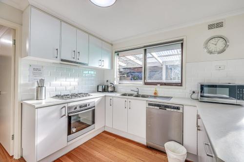 a kitchen with white cabinets and a clock on the wall at StayAU Newly Modern Comforts 3BRM Home Cranbourne in Cranbourne