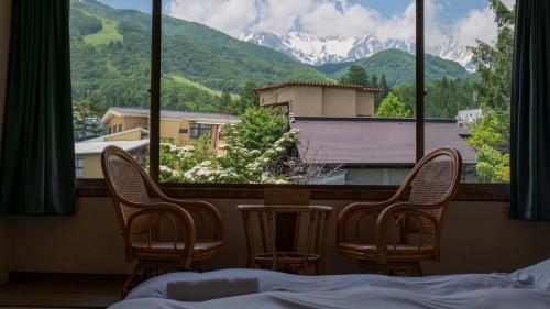 a room with three chairs and a view of a mountain at Hakuba Hospitality Inn YUKINOSO in Hakuba