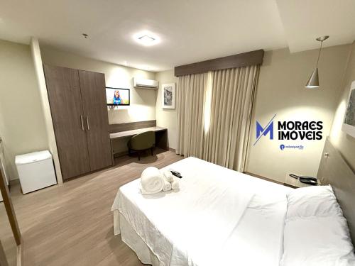 a hotel room with a white bed and a desk at Mont Blanc Suítes - Nova Iguaçu - Rio de Janeiro in Nova Iguaçu