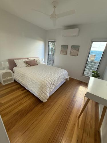 a white bedroom with a bed and a wooden floor at Beach house at Bangalee in Farnborough