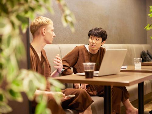 two men sitting at a table with a laptop at Anshin Oyado Woman&Man Nagoya Sakae in Nagoya