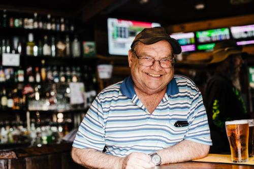 an older man sitting at a bar with a glass of beer at The Centennial Hotel Gulgong in Gulgong