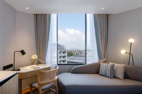 a room with a couch and a desk and a window at Novotel Rayong Star Convention Centre in Rayong