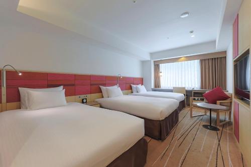 a hotel room with two beds and a desk at JR Kyushu Hotel Blossom Hakata Central in Fukuoka