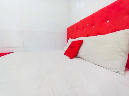 a white bed with a red headboard and white pillows at RedDoorz at Griya Jeniee Near Stadion Wilis Madiun in Madiun