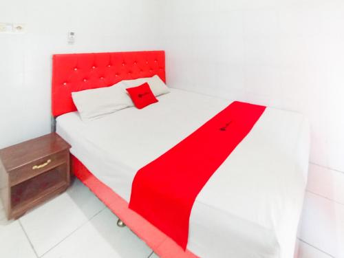 a red and white bed with a red blanket on it at RedDoorz at Griya Jeniee Near Stadion Wilis Madiun in Madiun