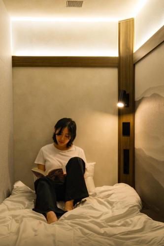 a woman sitting on a bed reading a book at GOYOO INN & cabins in Seoul