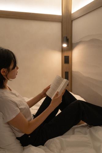 a woman sitting on a bed reading a book at GOYOO INN & cabins in Seoul