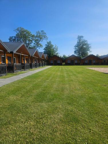 a large grass field in front of a row of houses at By The Way - domki nad morzem in Paprotno