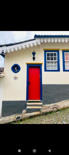 a red door on a white house with blue windows at Cantinho Ideal Casal in Ouro Preto