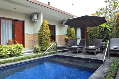 a pool with chairs and an umbrella next to a house at Cening Ayu Sanur in Sanur