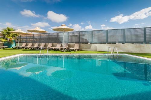 a swimming pool with chairs and umbrellas next to a building at Occidental Murcia Agalia in Murcia