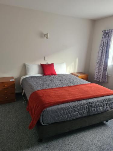 a bedroom with a bed with a red pillow on it at Arran Motel in Te Anau