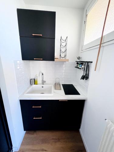 - une cuisine avec un évier blanc et des placards noirs dans l'établissement Studio cosy 80 m de la plage, à Cabourg