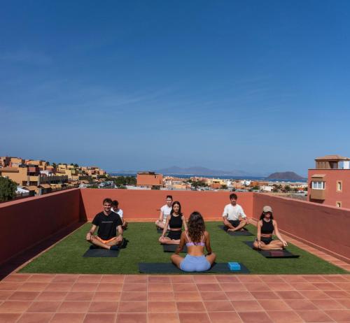 a group of people sitting in a yoga pose on a roof at Banama Coliving & Coworking, Surf & Yoga - Casa Roja in Corralejo