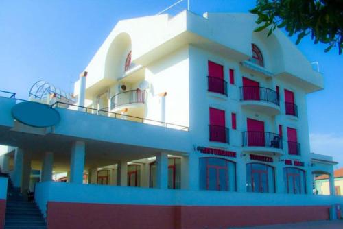 a white building with red windows and stairs in front at Hotel Lungomare Brancaleone in Brancaleone Marina