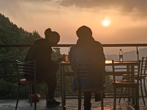 two people sitting at a table watching the sunset at Amazing view Home Stay in McLeod Ganj