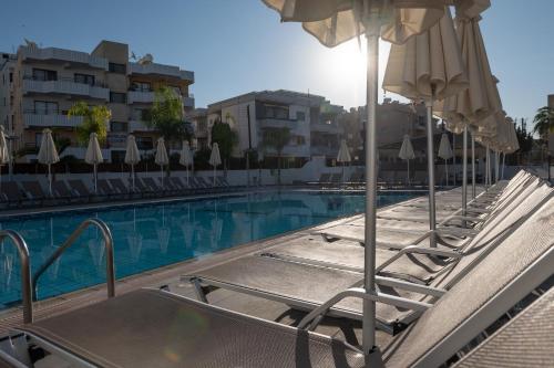 a swimming pool with lounge chairs and umbrellas at Kefalos Damon Hotel Apartments in Paphos City