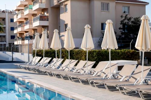 a row of white chairs and umbrellas next to a swimming pool at Kefalos Damon Hotel Apartments in Paphos City