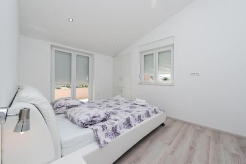 a white bedroom with a bed and two windows at Apartment Stipan in Bibinje