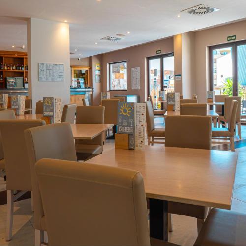 a restaurant with wooden tables and chairs and windows at Ohtels Campo De Gibraltar in La Línea de la Concepción