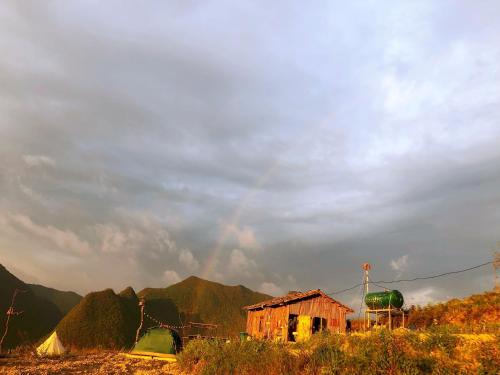 a rainbow in the sky over a house and mountains at Sunrise Camping Ha Giang Lung Cu in Ha Giang